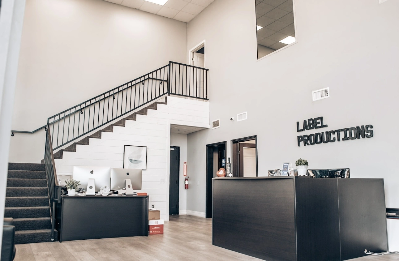 The lobby of Label Productions in Murrieta, California, featuring a spacious, open area with modern décor. The lobby includes a sleek reception desk and comfortable seating. A set of stairs leads up to the second floor, with a stylish railing and bright lighting enhancing the space.
